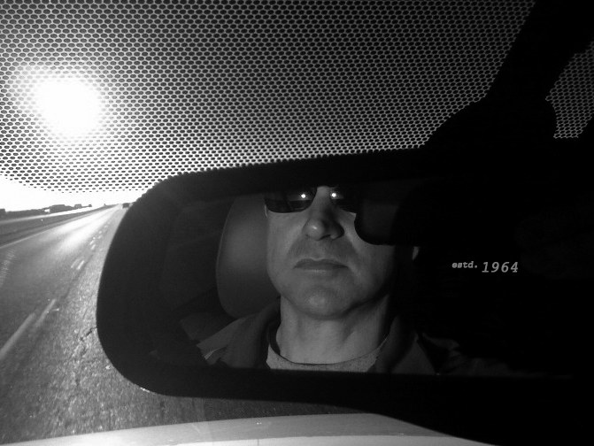 Michael Chaffin reflected in a rearview mirror on an open highway at sunrise
